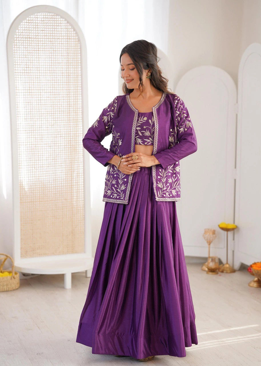 Woman wearing a purple traditional outfit with intricate patterns in a minimalistic room.